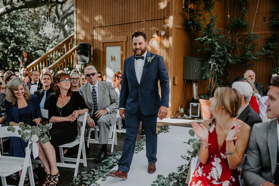 Groom in navy suit walks down aisle at outdoor wedding ceremony