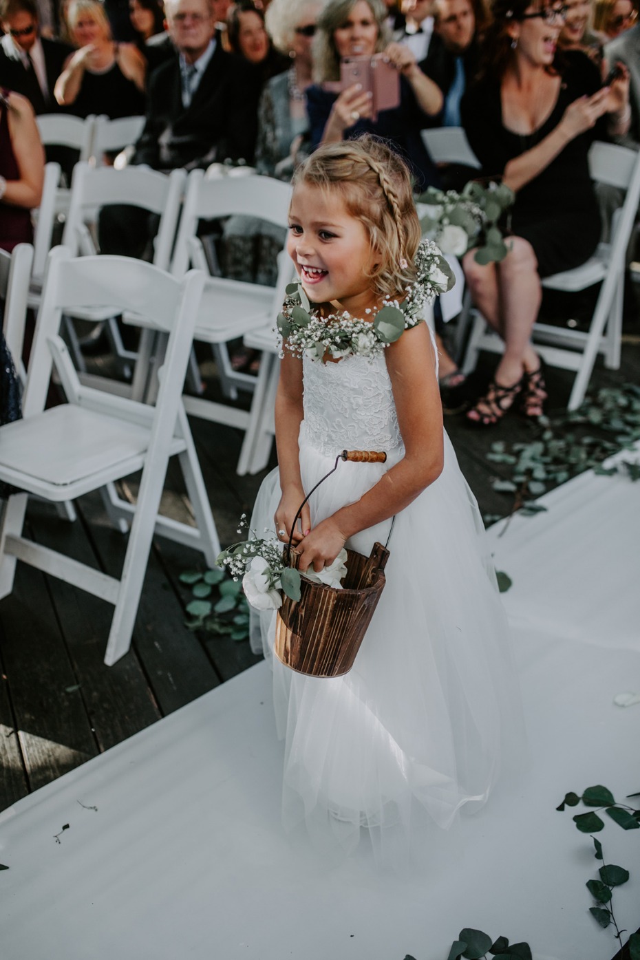 Smiling flower girl in a white dress at an outdoor wedding