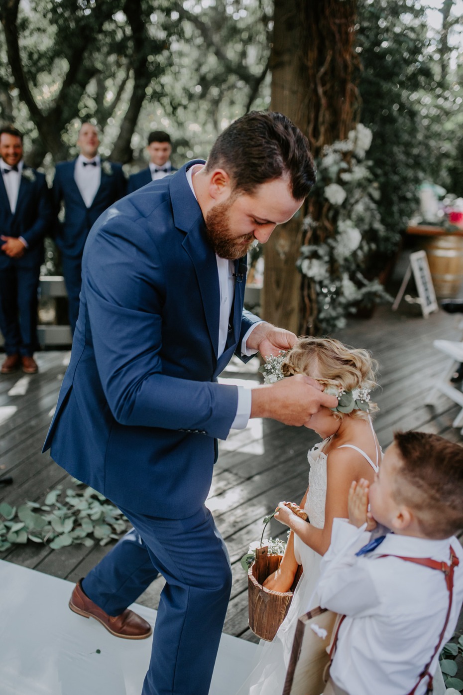 groom helping the flower girl with her flower halo