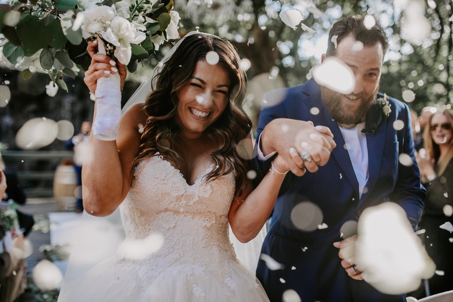 Newly married couple laughing under confetti after the wedding ceremony