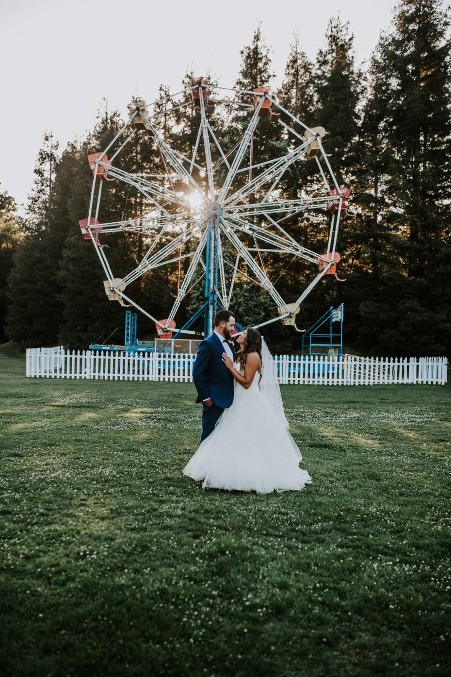 Newlyweds embrace in front of a Ferris wheel at their wedding