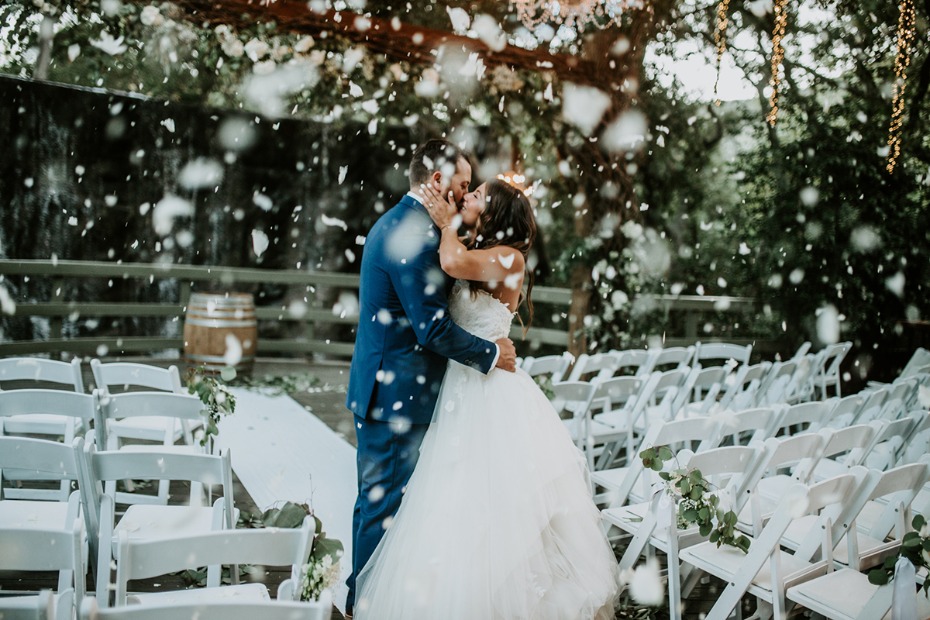 Romantic wedding couple kissing amidst falling confetti with chairs