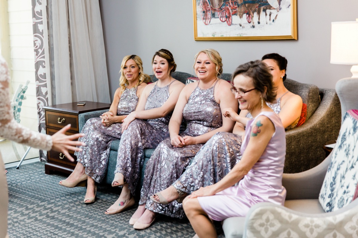 Bridesmaids laugh as bride shows dress on wedding day