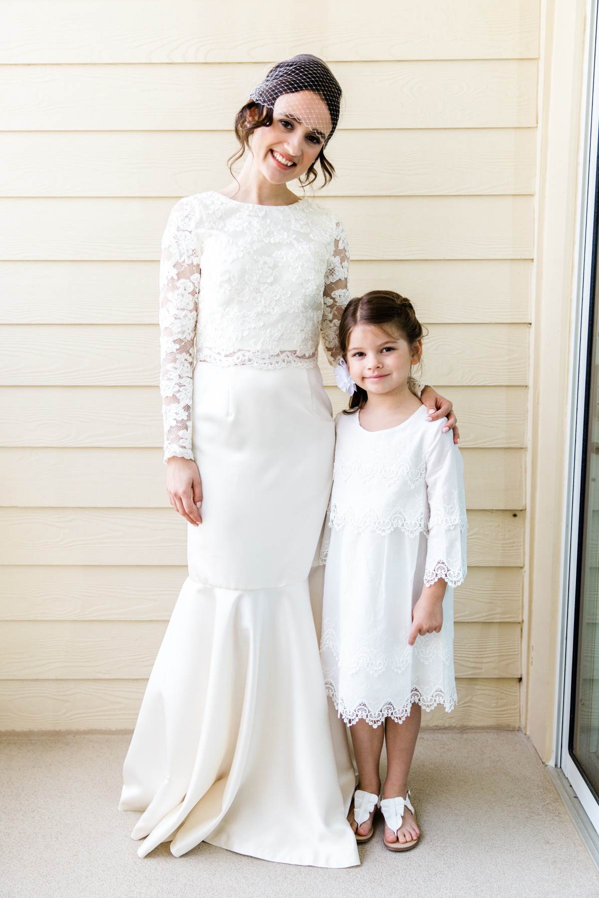 Smiling bride and daughter pose in white dresses outdoors
