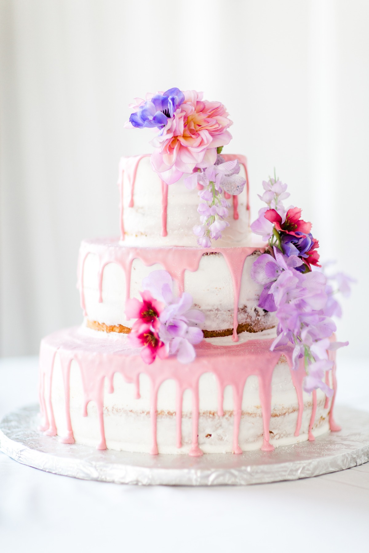 Three-tiered floral cake with pink drip and vibrant flowers