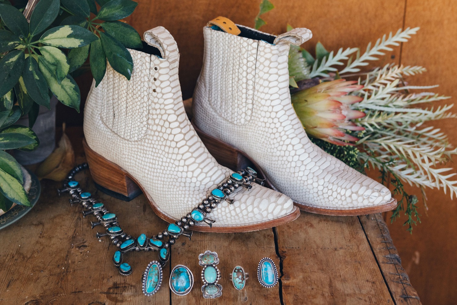 White snakeskin boots with turquoise jewelry on wooden surface