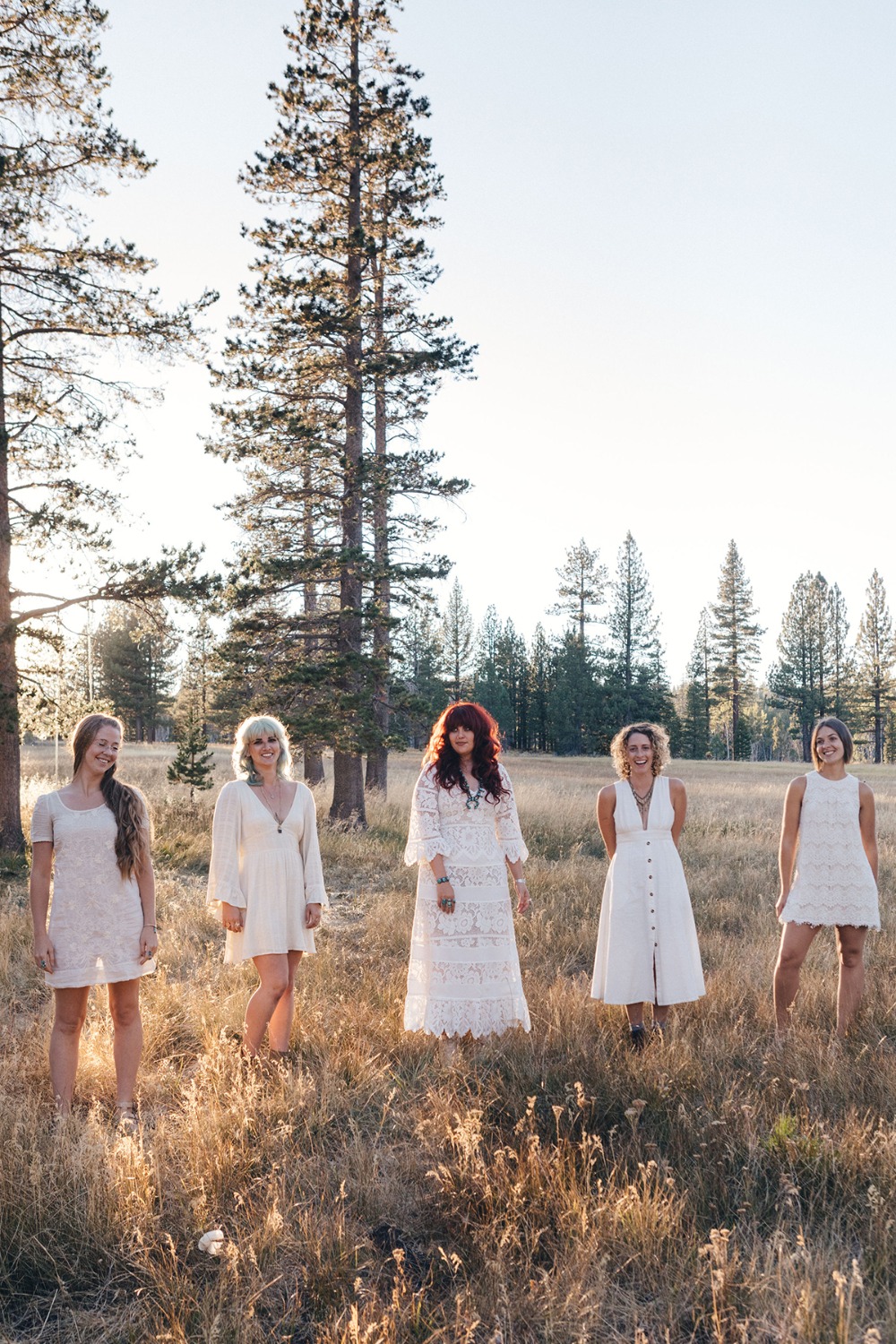 Women in white dresses standing in a field near tall trees