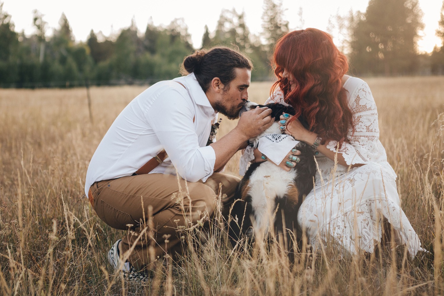 Newlyweds kissing their dog in a golden field at sunset