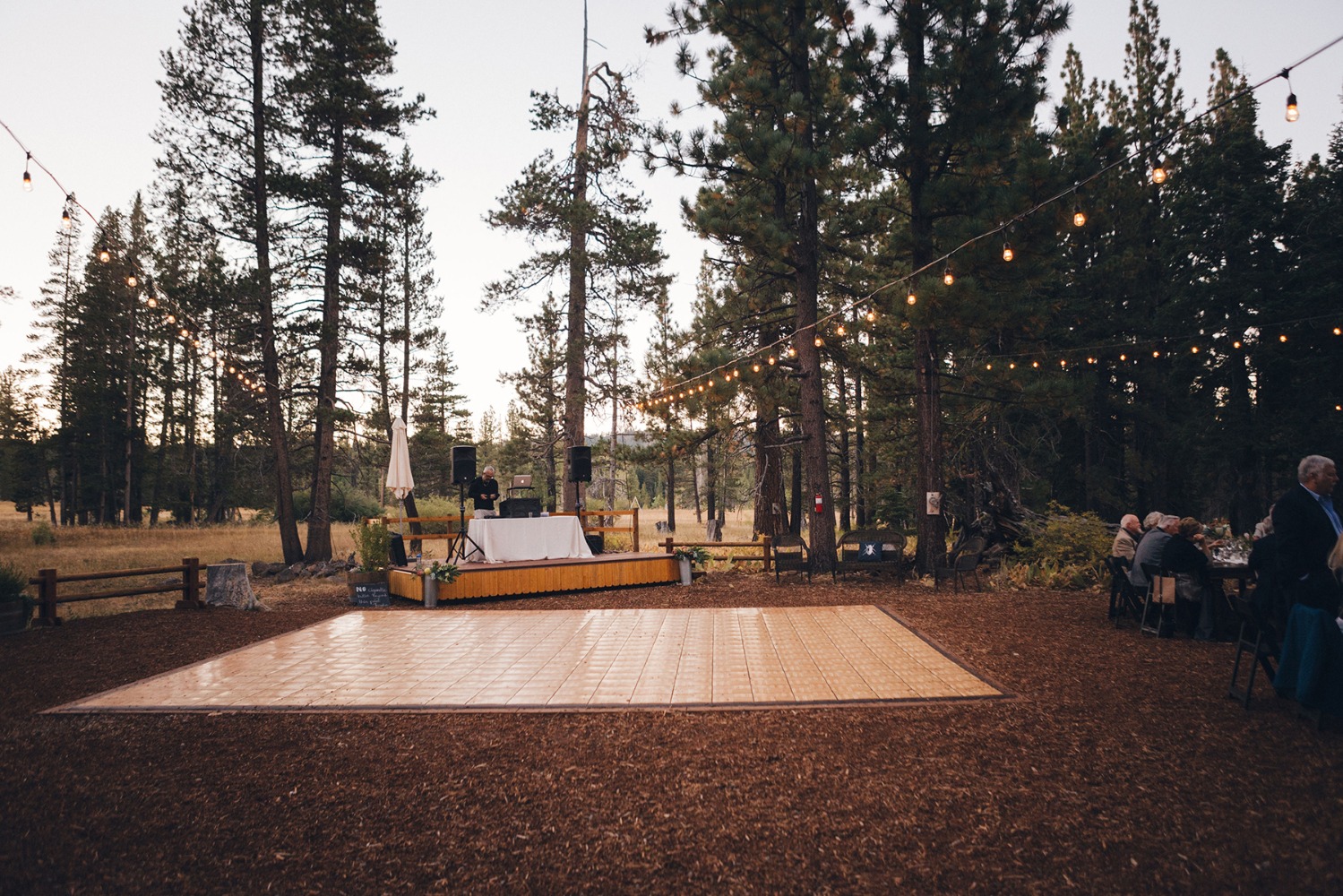 Outdoor event with dance floor and DJ setup in a forest setting