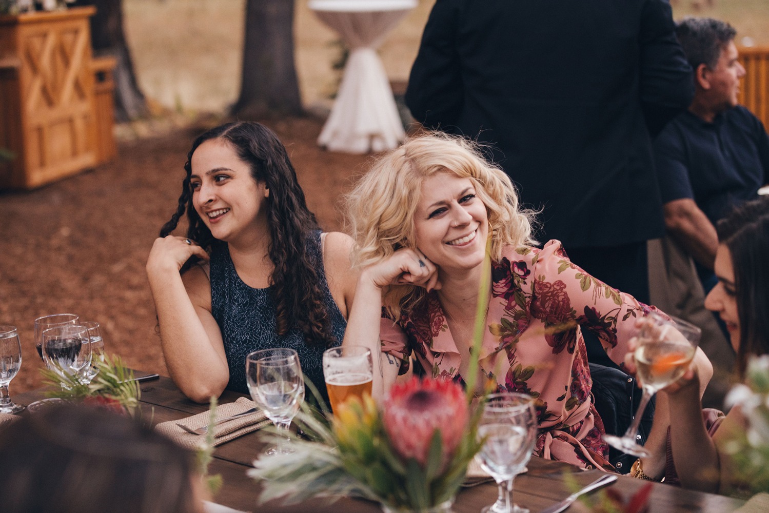 Two happy women smiling at a table with drinks and flowers