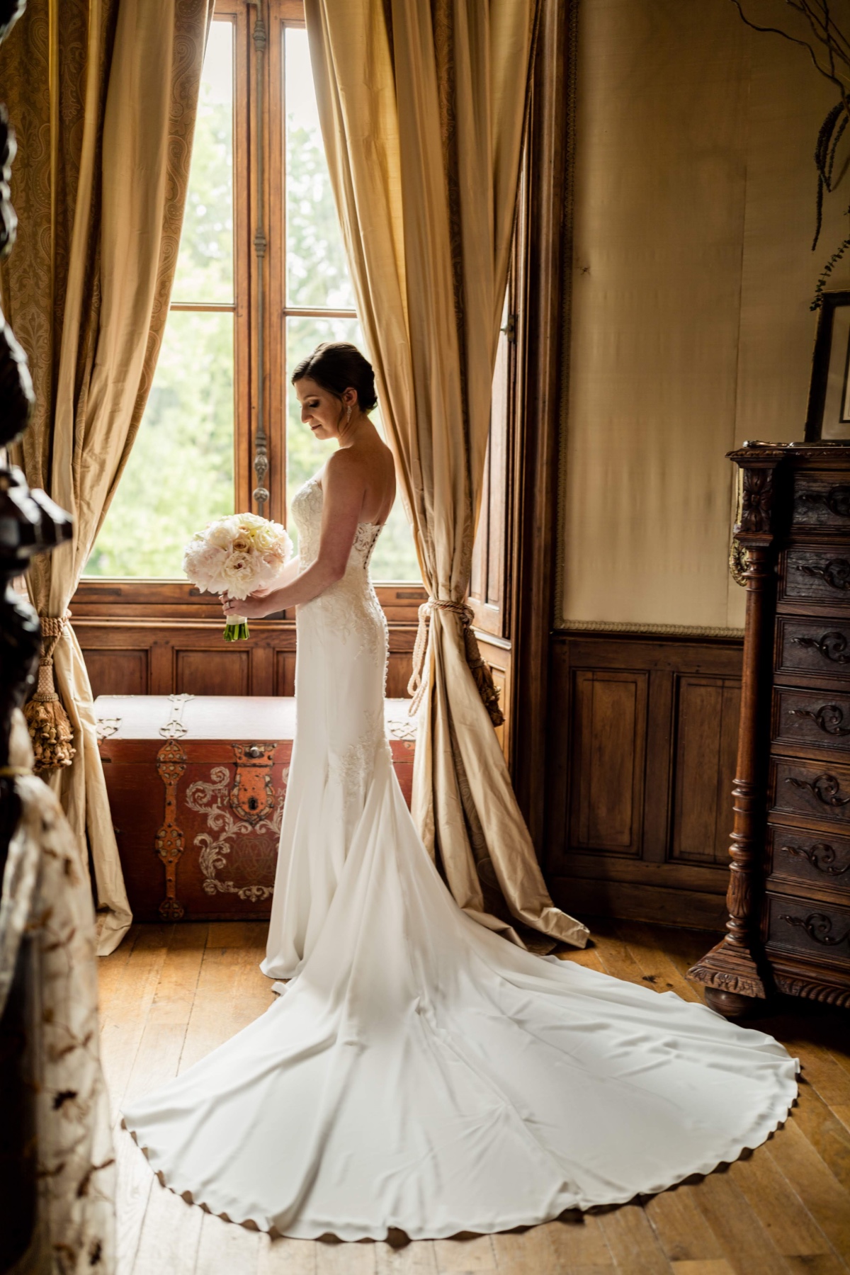 Bride in white dress holding bouquet by window light
