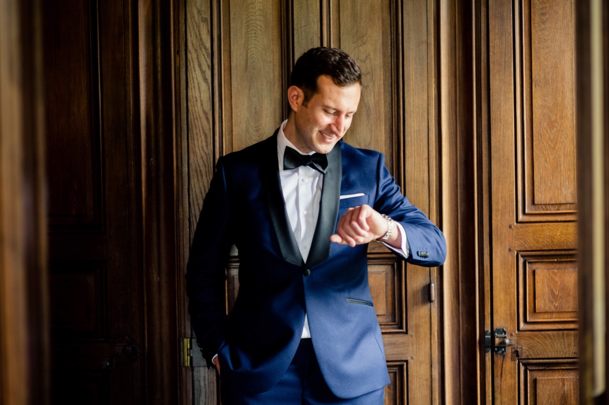 Groom in blue tuxedo checking watch before wedding