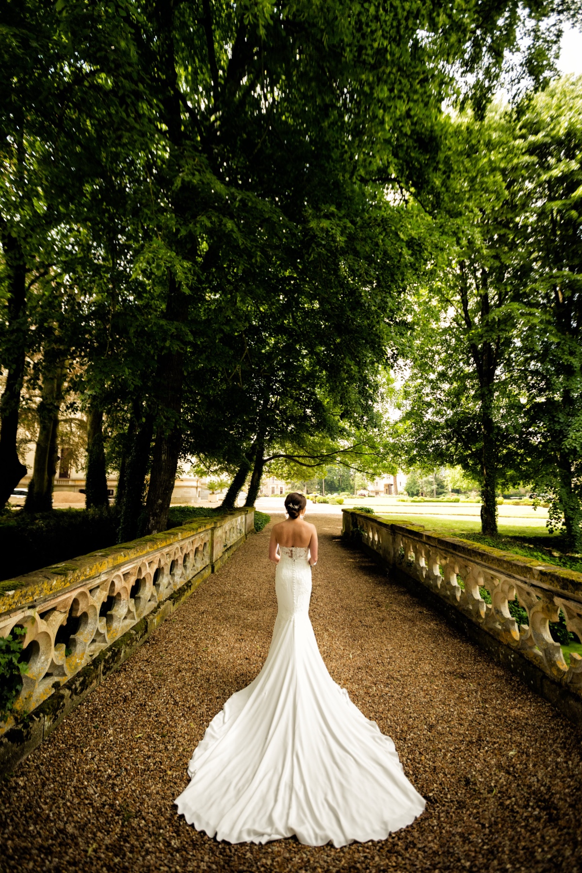 Bride walks away on stone path lined with green trees