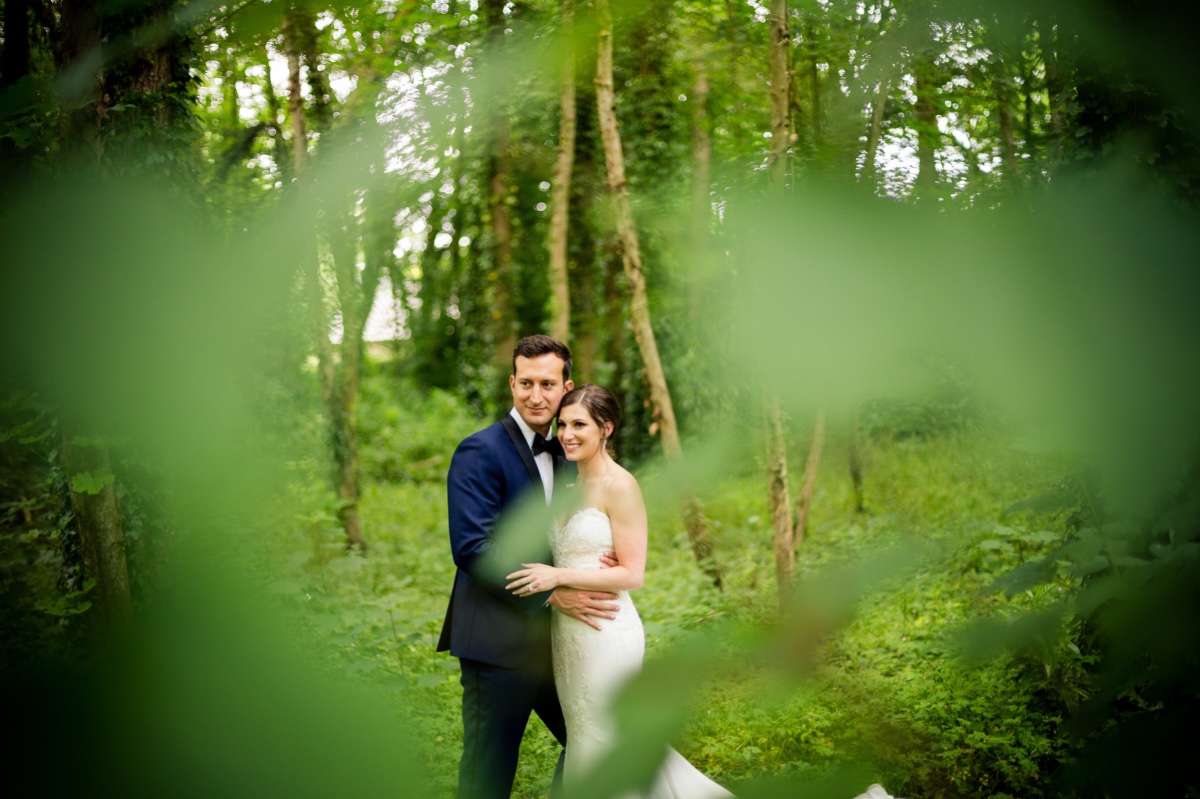 Newlyweds embrace in a forest wedding photo framed by leafy foliage