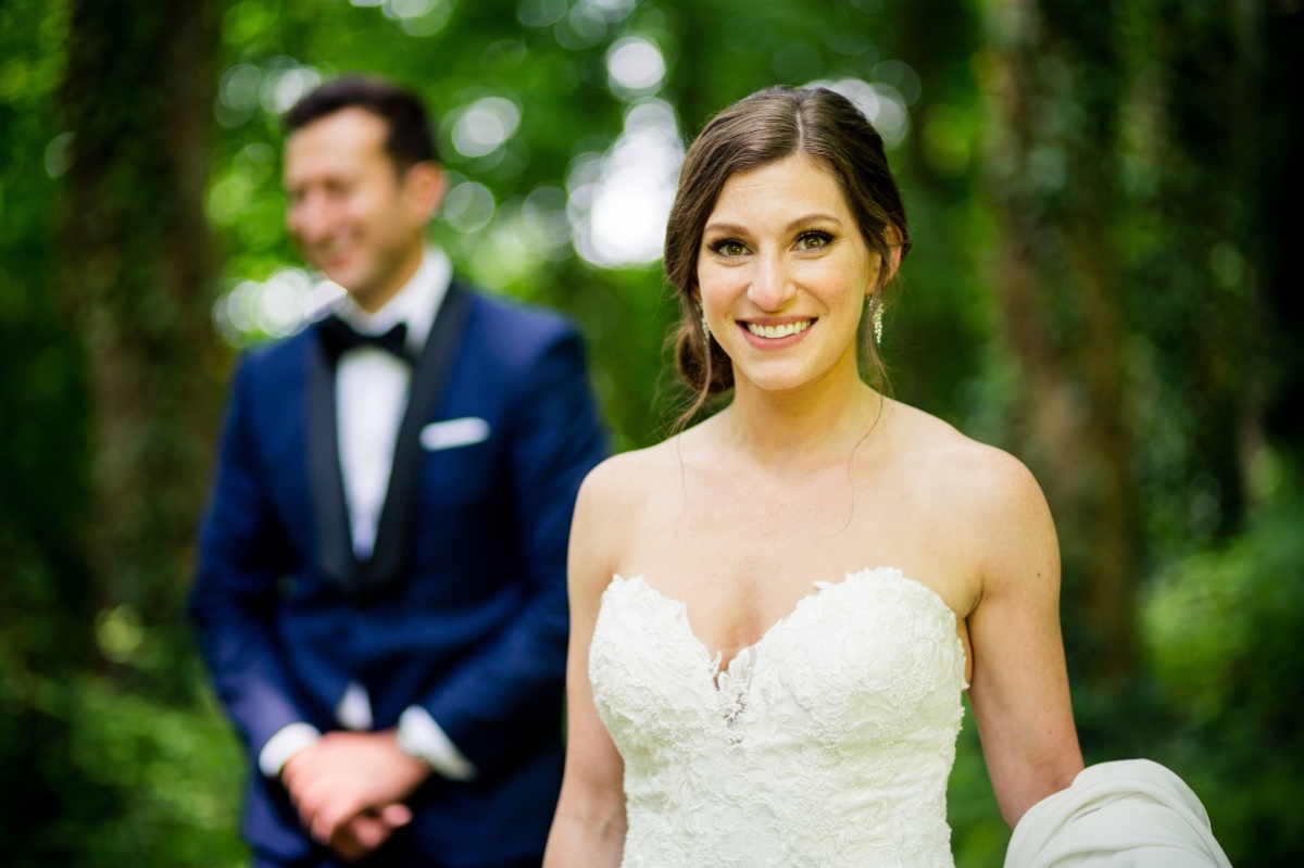 Smiling bride in a white dress with groom in blue suit in the background