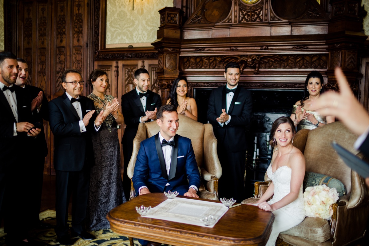 Bride and groom smile with guests clapping at a wedding ceremony