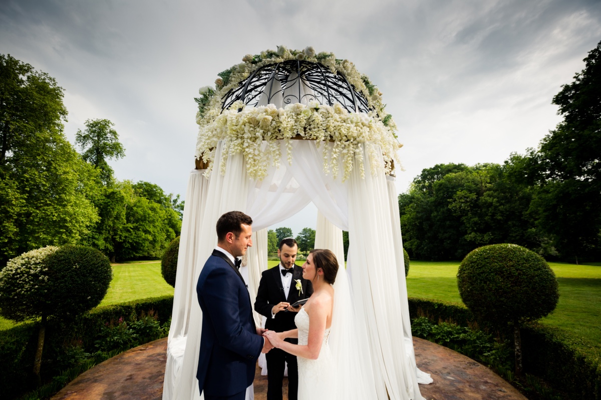 Wedding ceremony with couple holding hands under floral arch