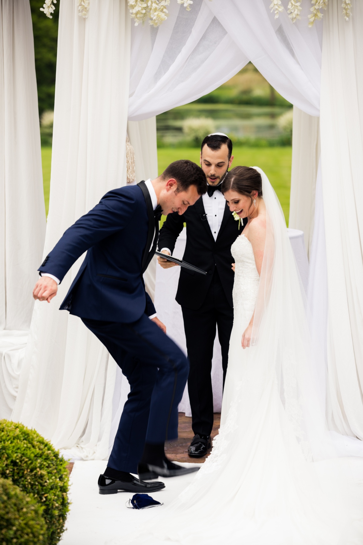 Groom stomping on glass at wedding ceremony, bride smiling, rabbi present