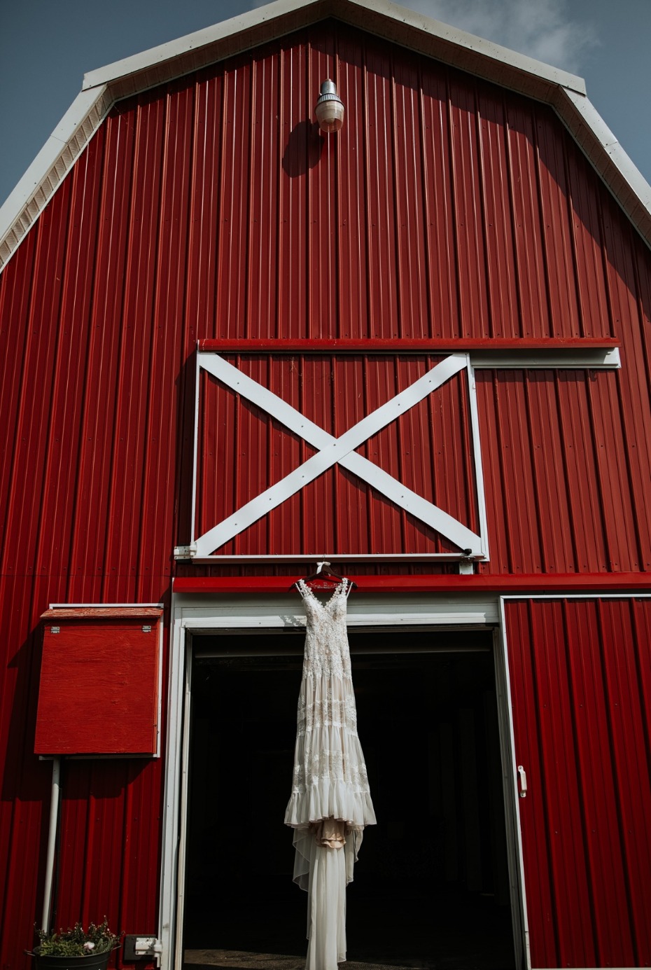 White wedding dress hanging on red barn door for wedding