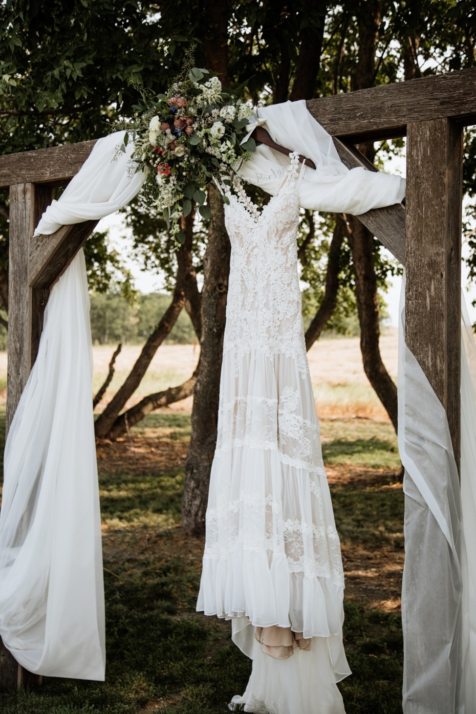 Elegant white wedding dress and flowers on wooden arch
