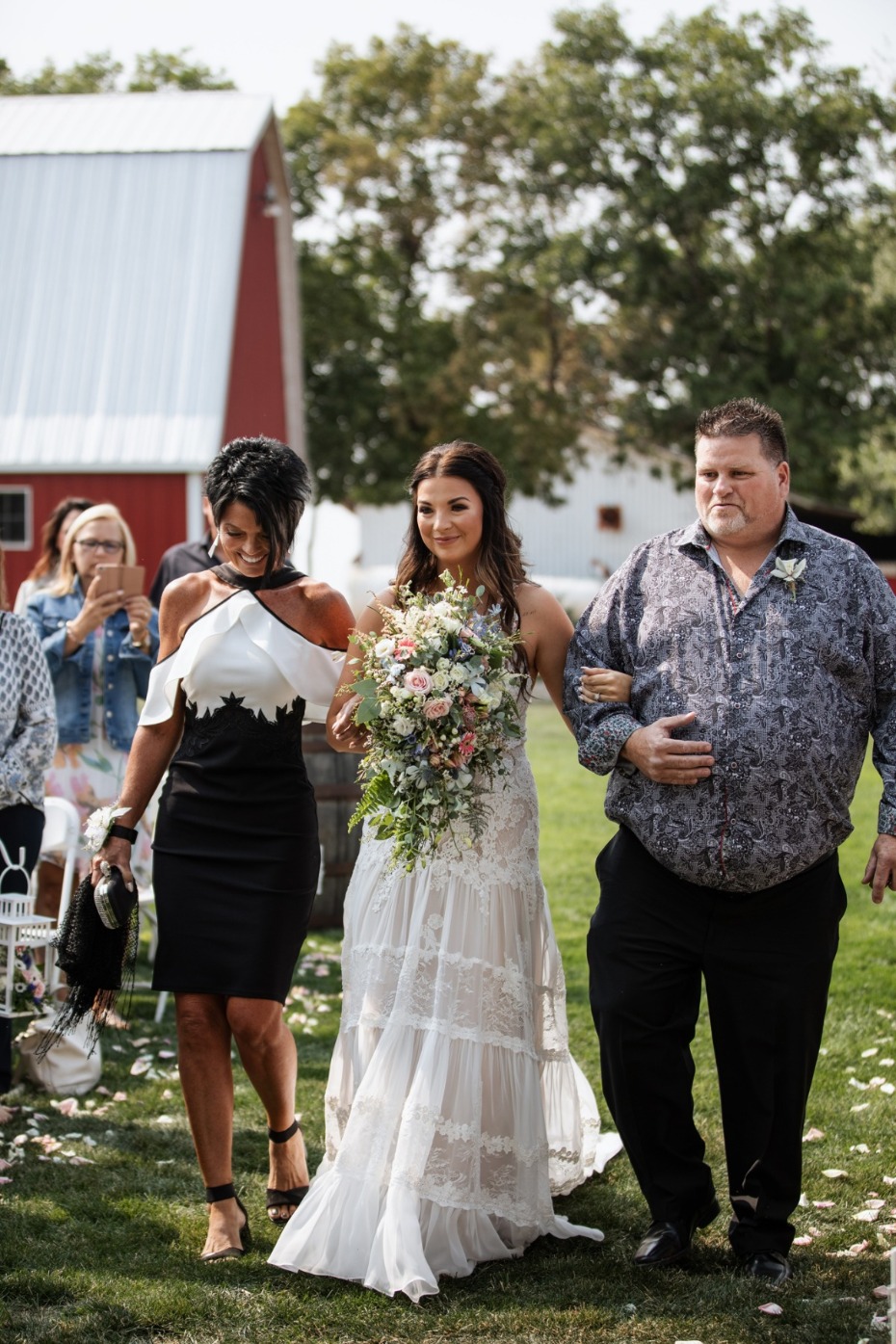 Bride and family walk aisle at outdoor barn wedding