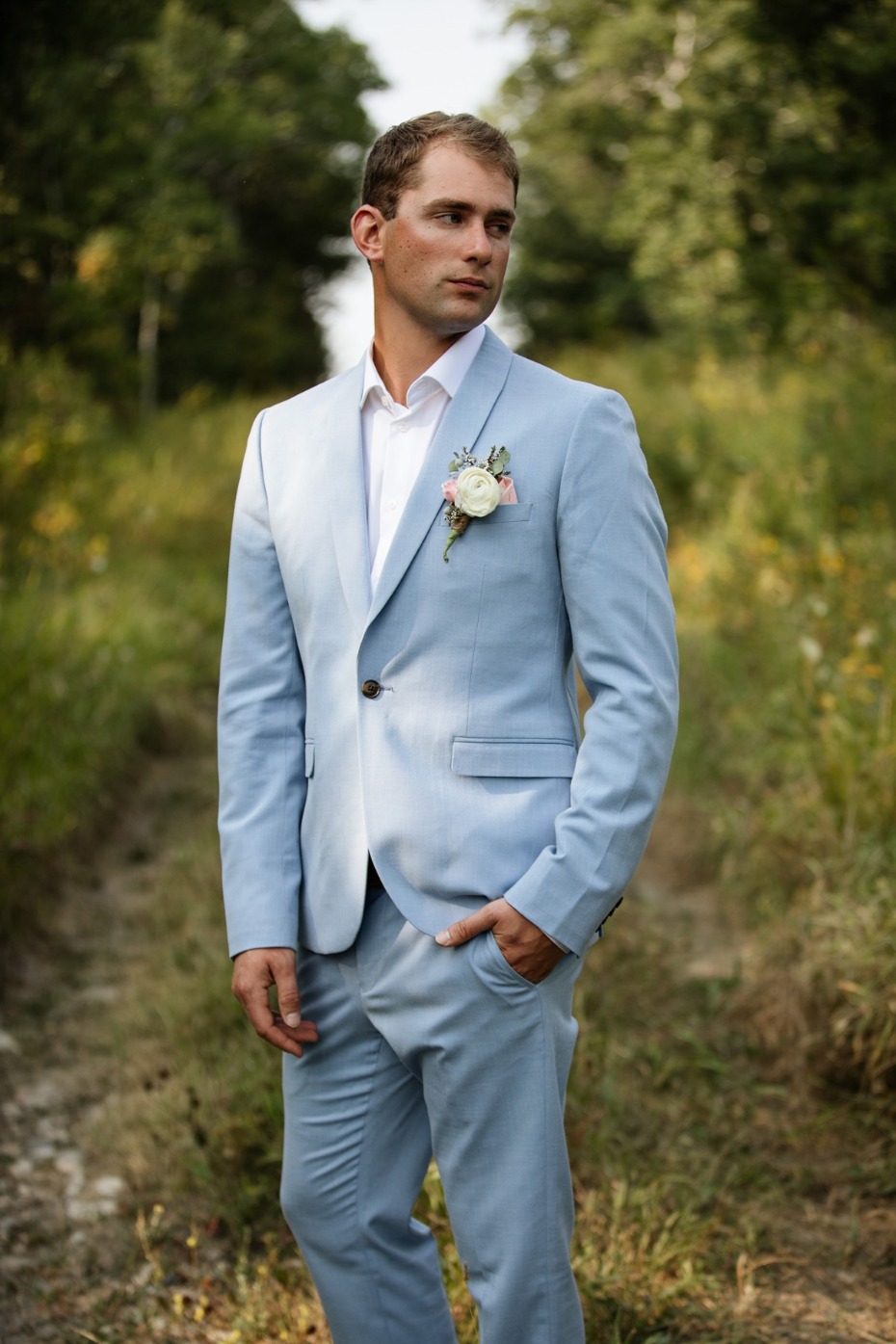 Groom in a light blue suit poses in nature, ready for his wedding