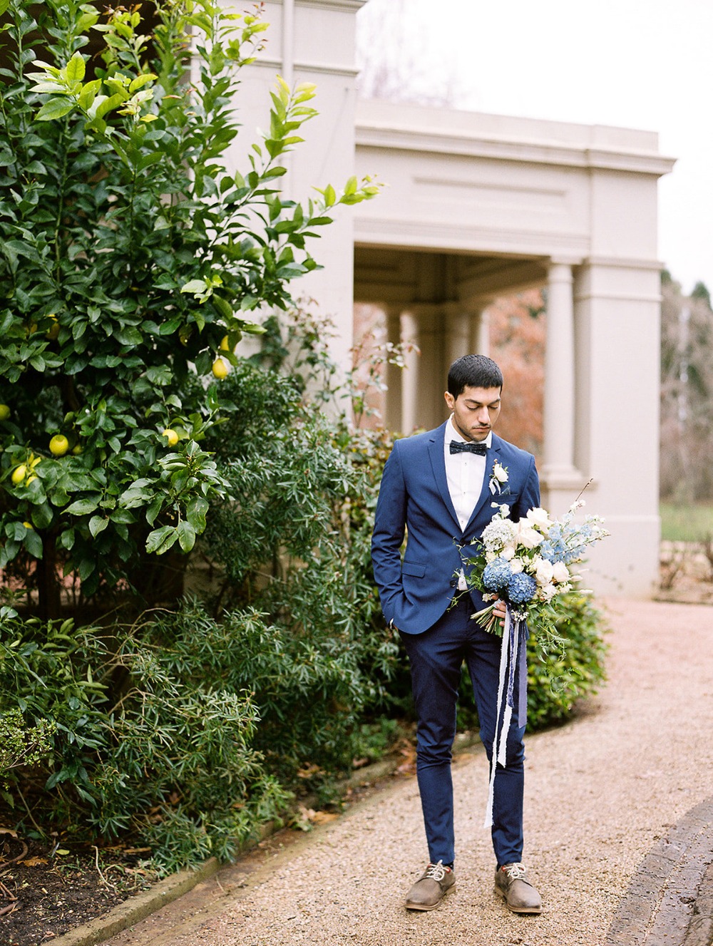 Groom in blue suit holding bouquet outside before wedding ceremony