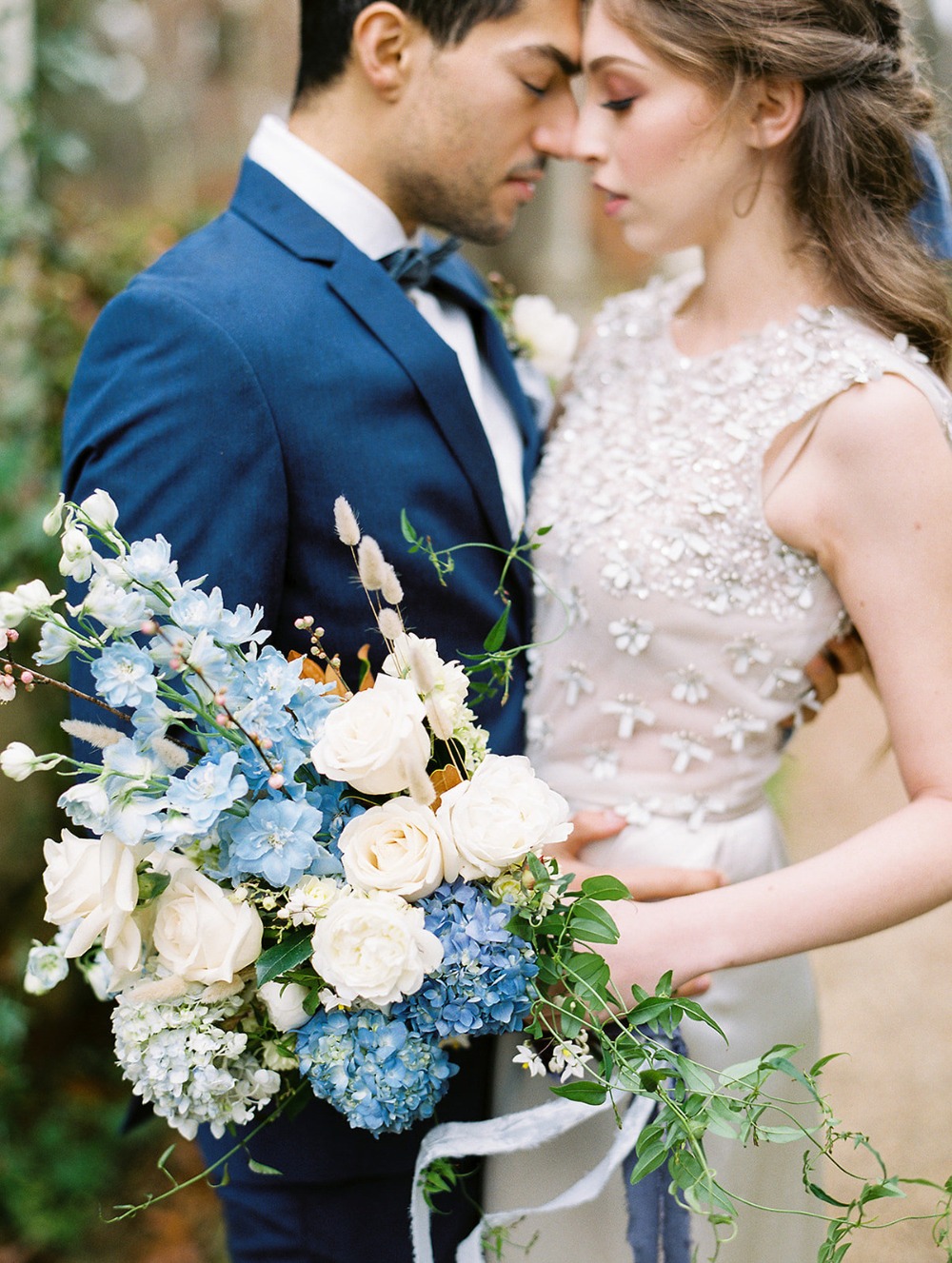 Bride and groom embrace, holding a blue and white bouquet