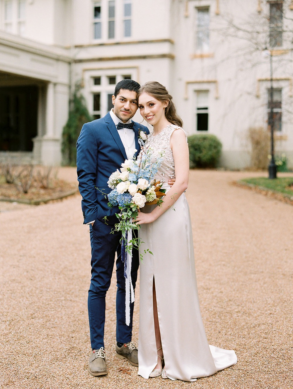 Happy wedding couple posing with bouquet at mansion