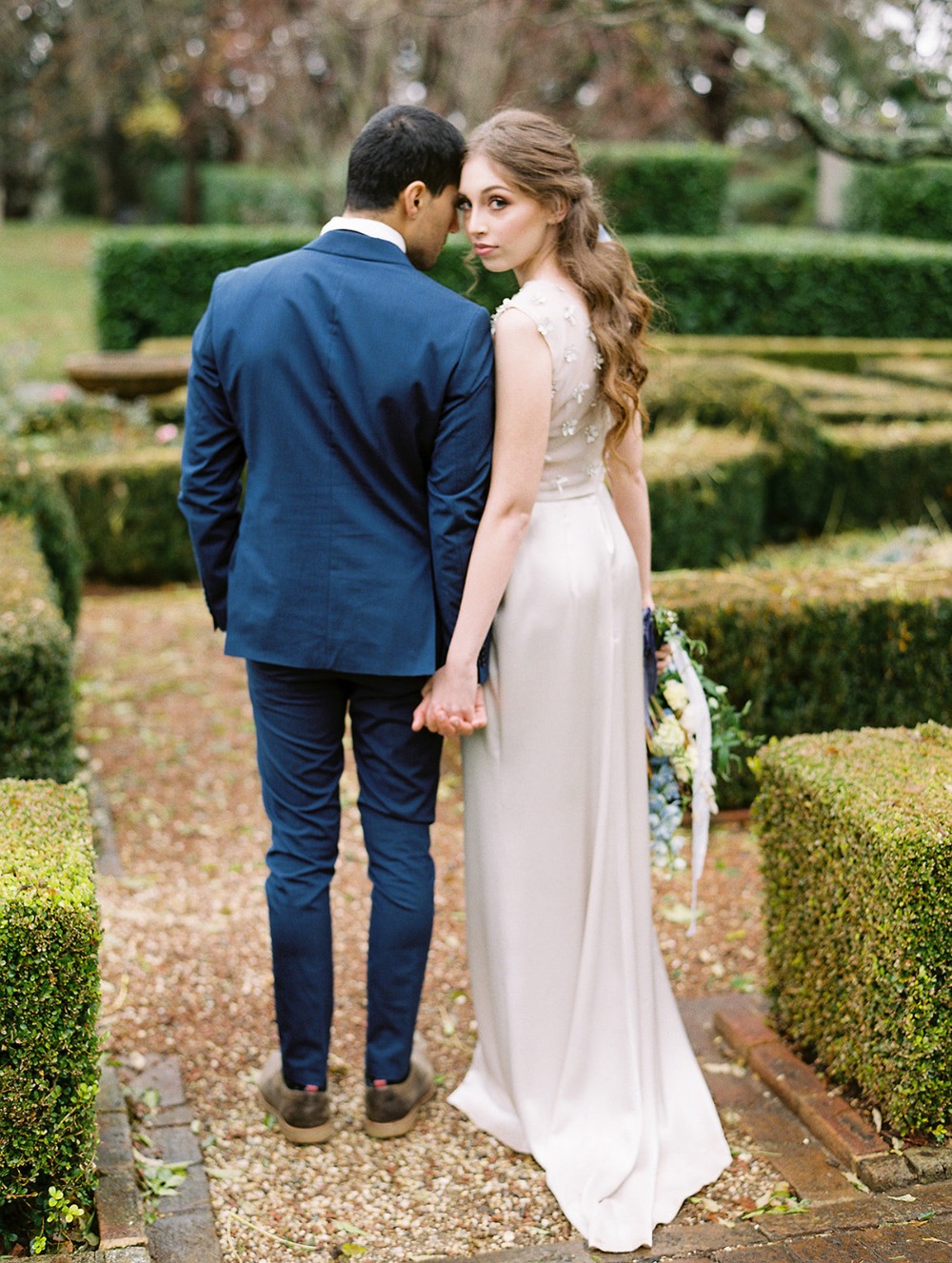 Bride and groom holding hands, back view in garden