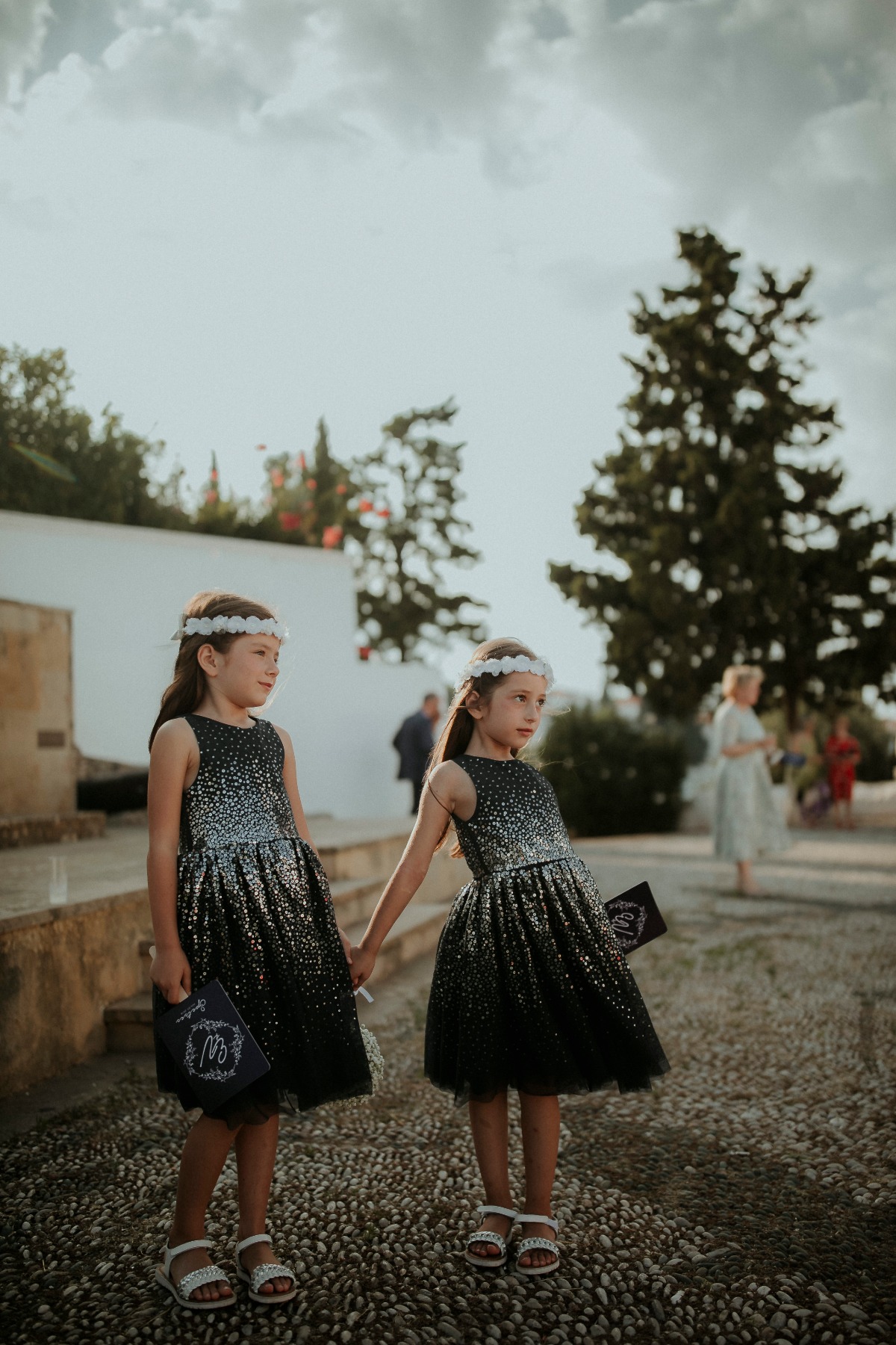 Two flower girls in dresses hold hands at outdoor wedding