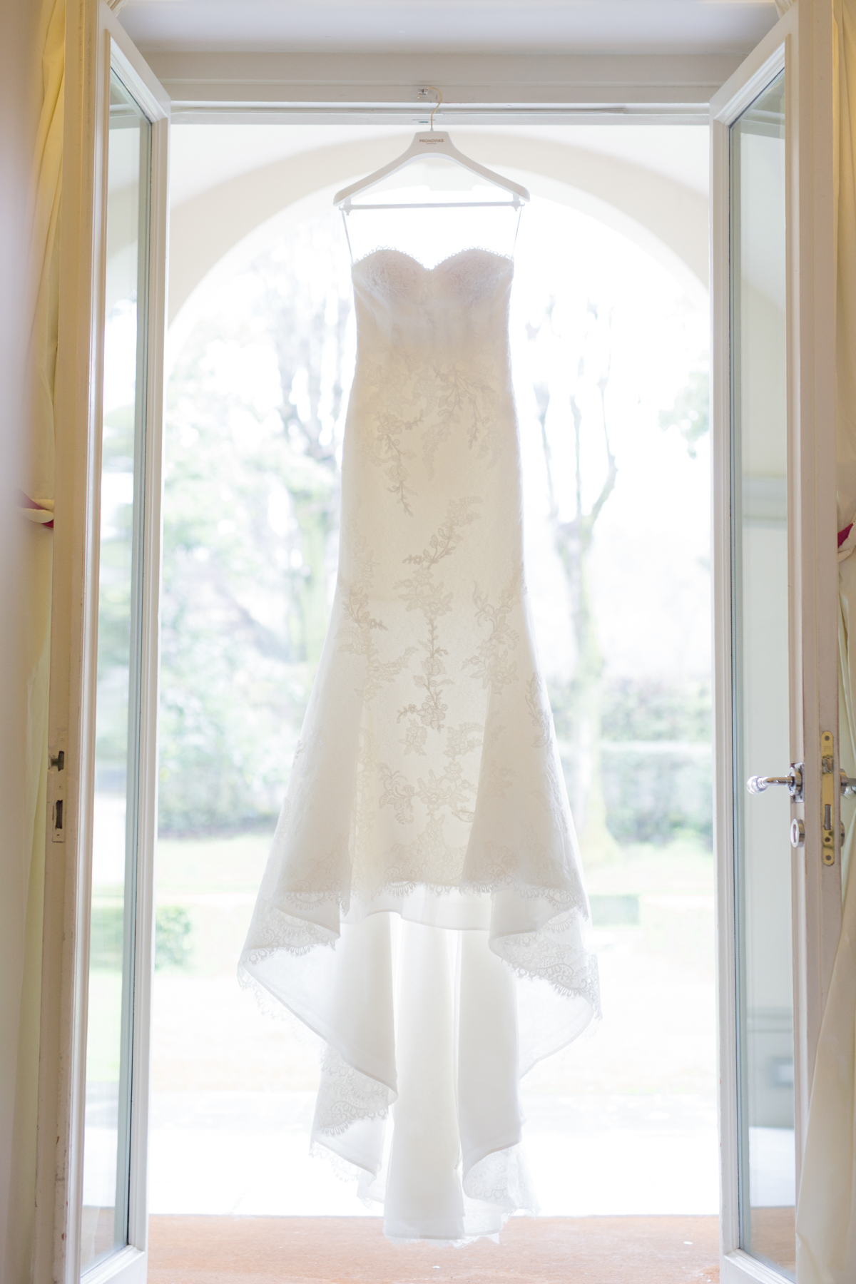 Elegant white wedding dress hanging in a bright doorway