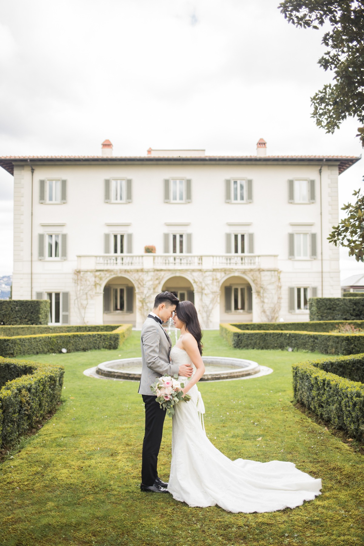 Elegant couple embraces in a garden before a grand estate on their wedding day