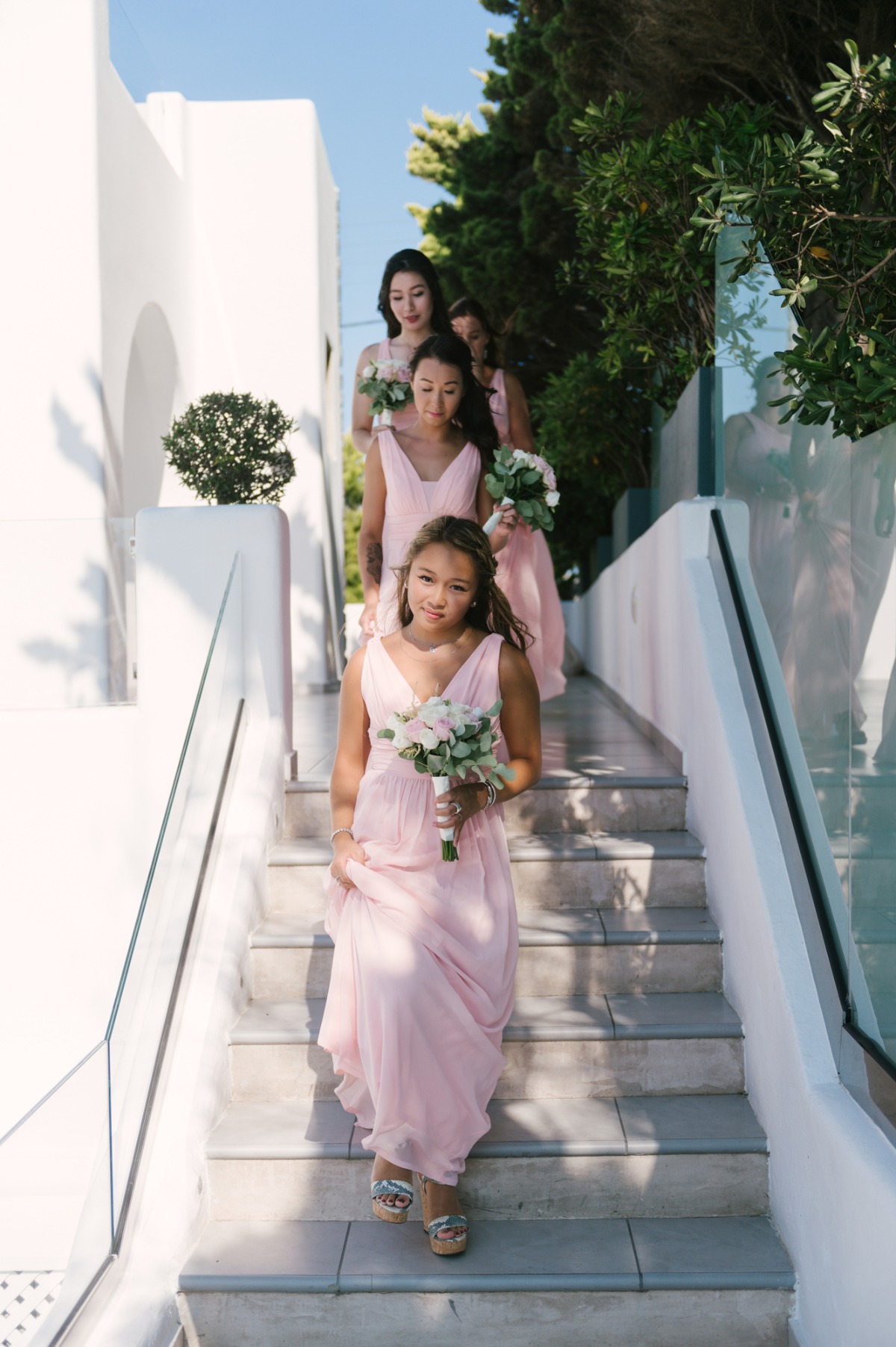 Bridesmaids in pink gowns walk down the white stairs