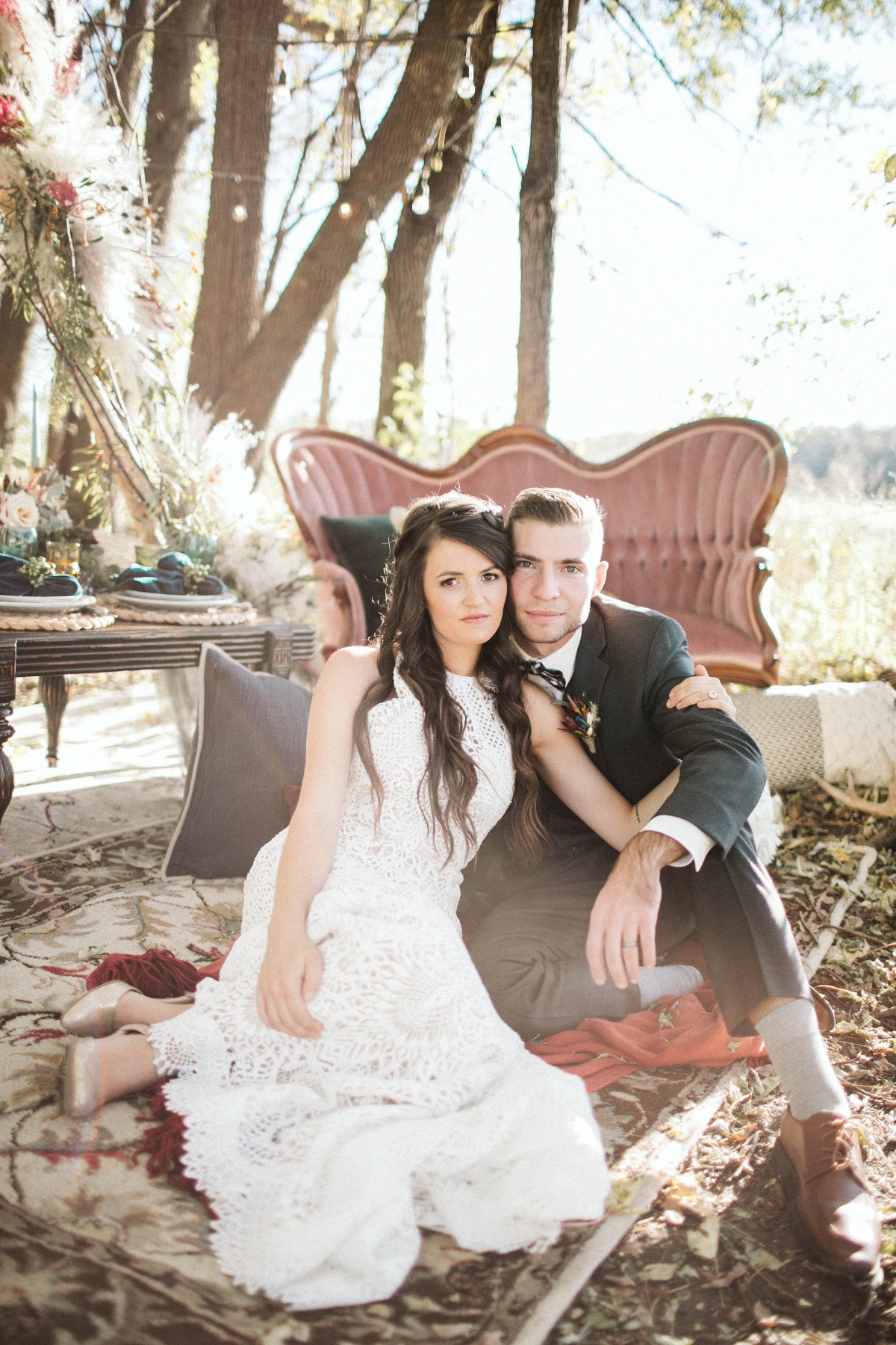 Bride and groom sitting outdoors on rug at wedding