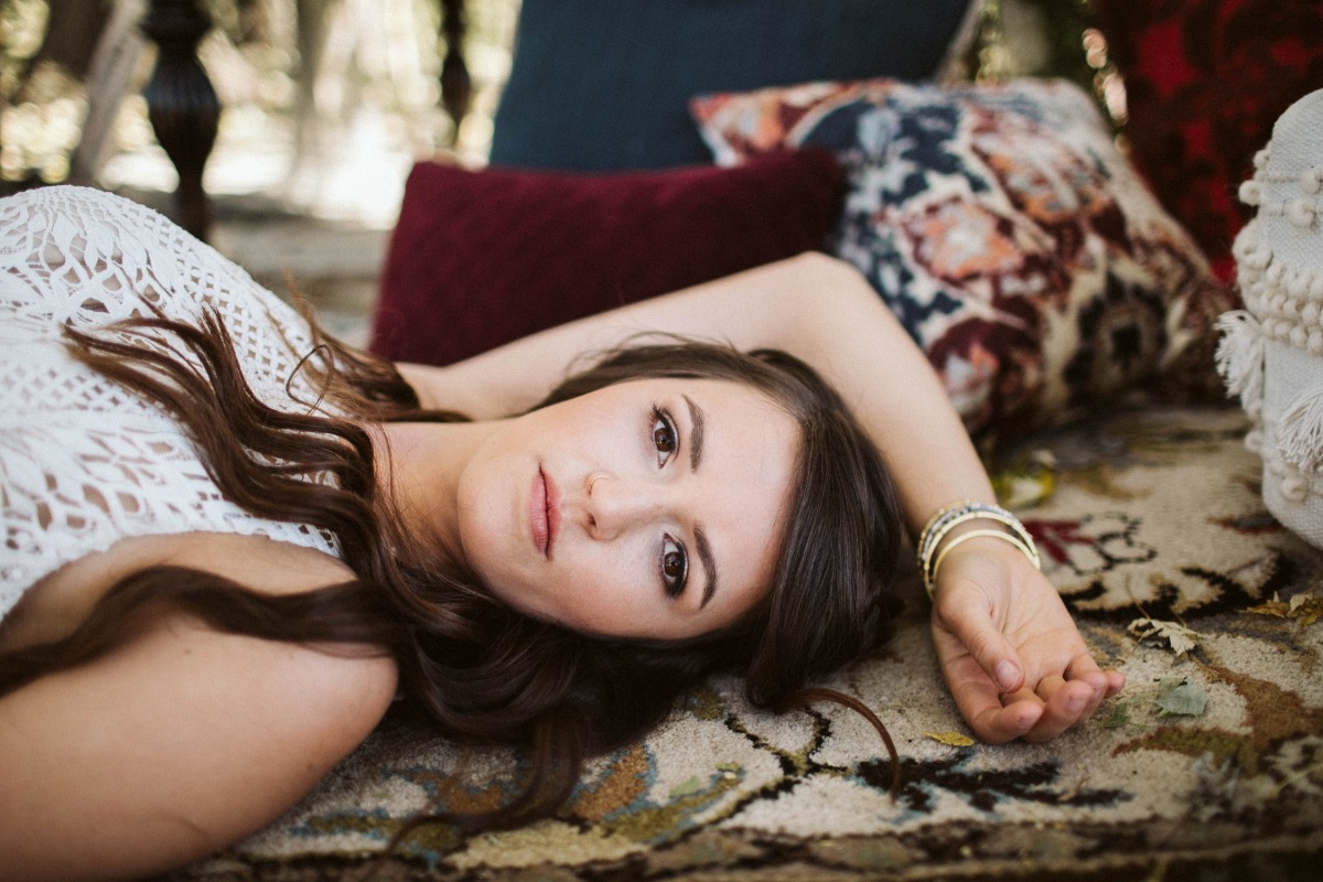 Brunette woman in white lace dress relaxes on boho pillows