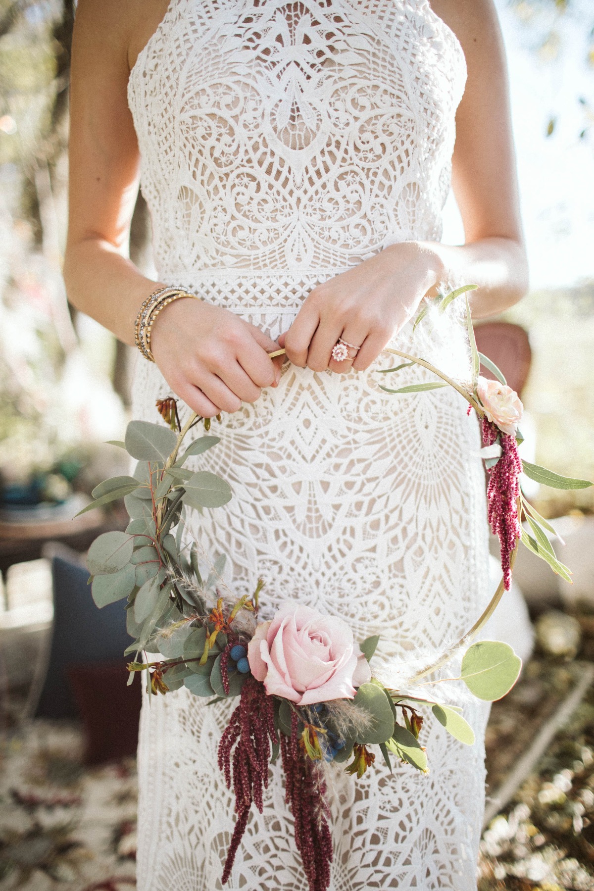 Bride in lace dress holds floral hoop wedding bouquet