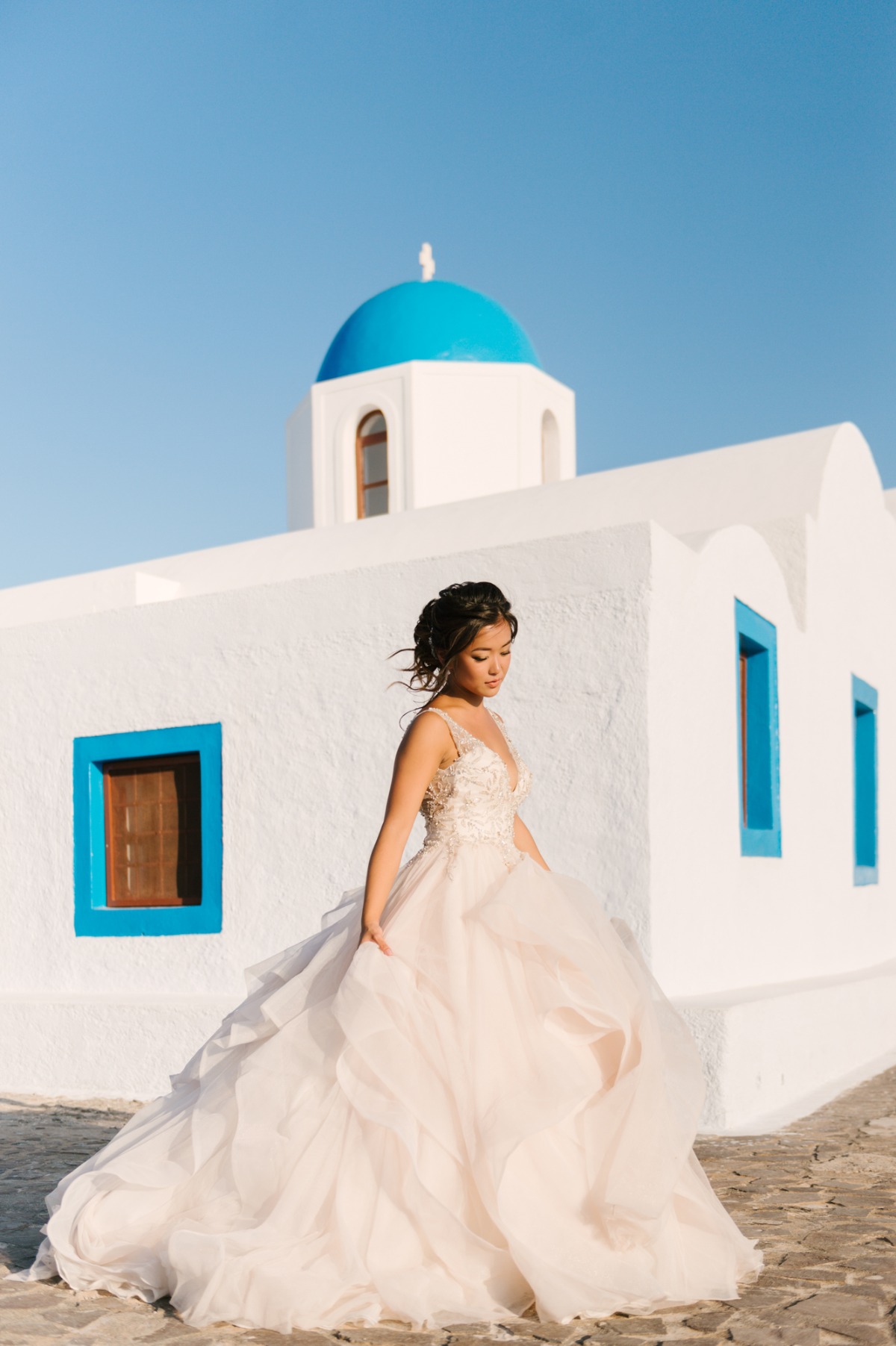 Elegant bride in gown poses near Greek church with blue dome