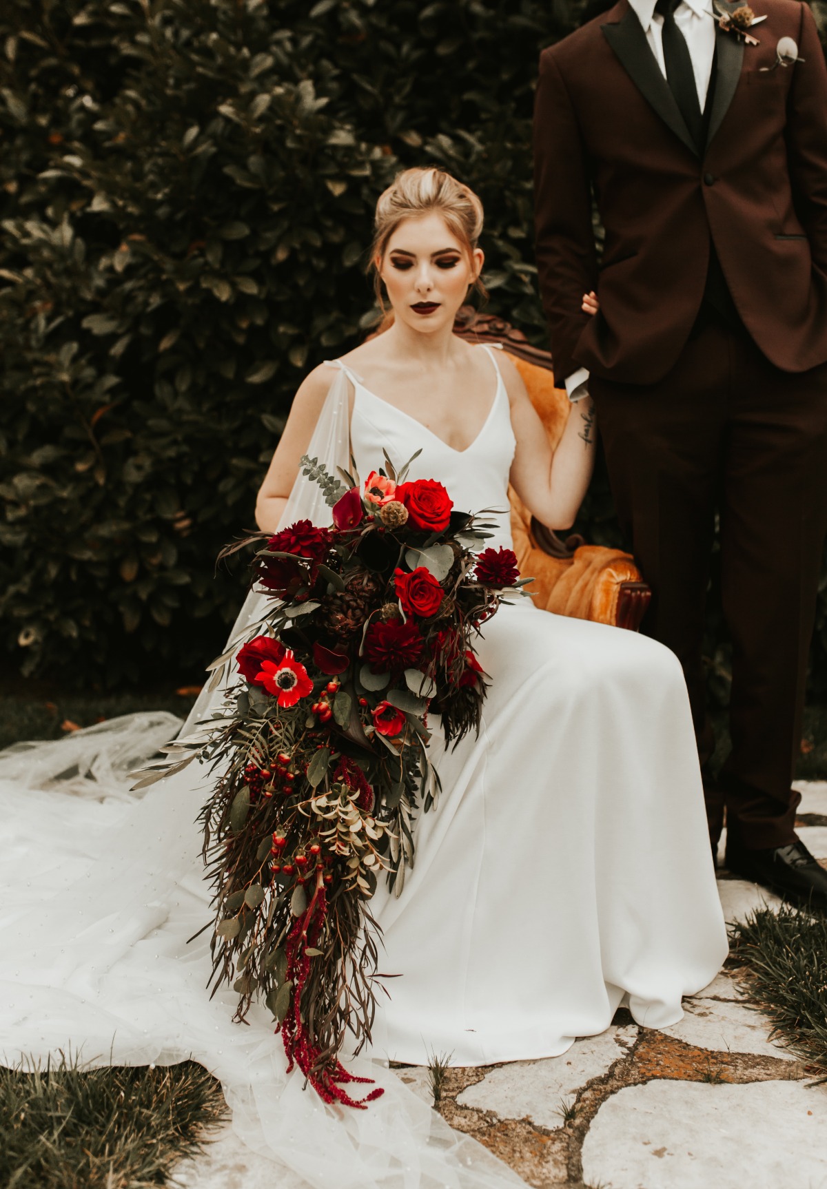 Bride in white dress holds cascade bouquet outdoors