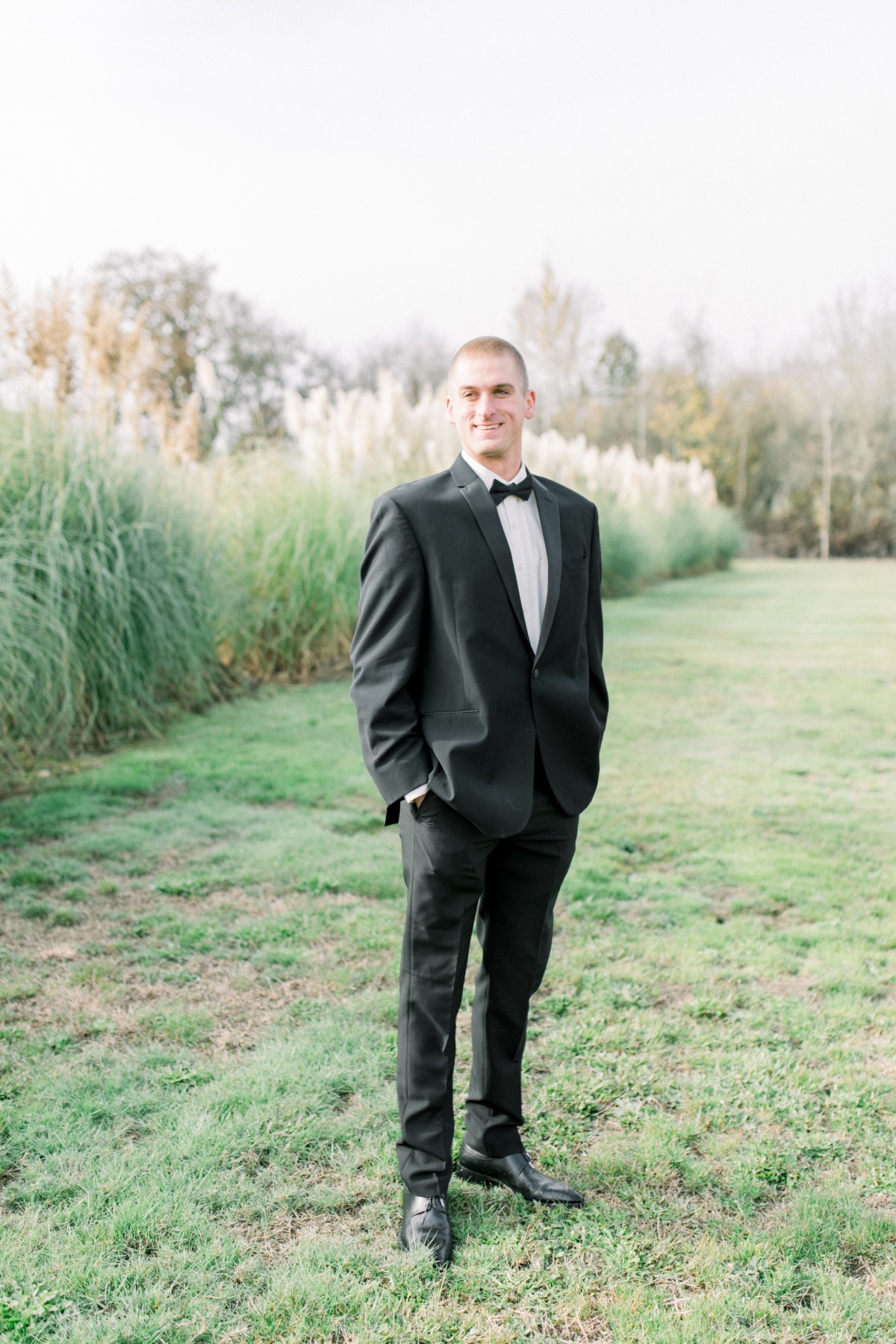 Smiling groom in black suit outdoor wedding setting