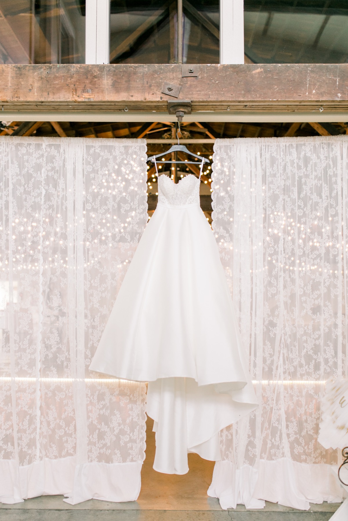 Elegant white bridal gown hangs lace curtain backdrop