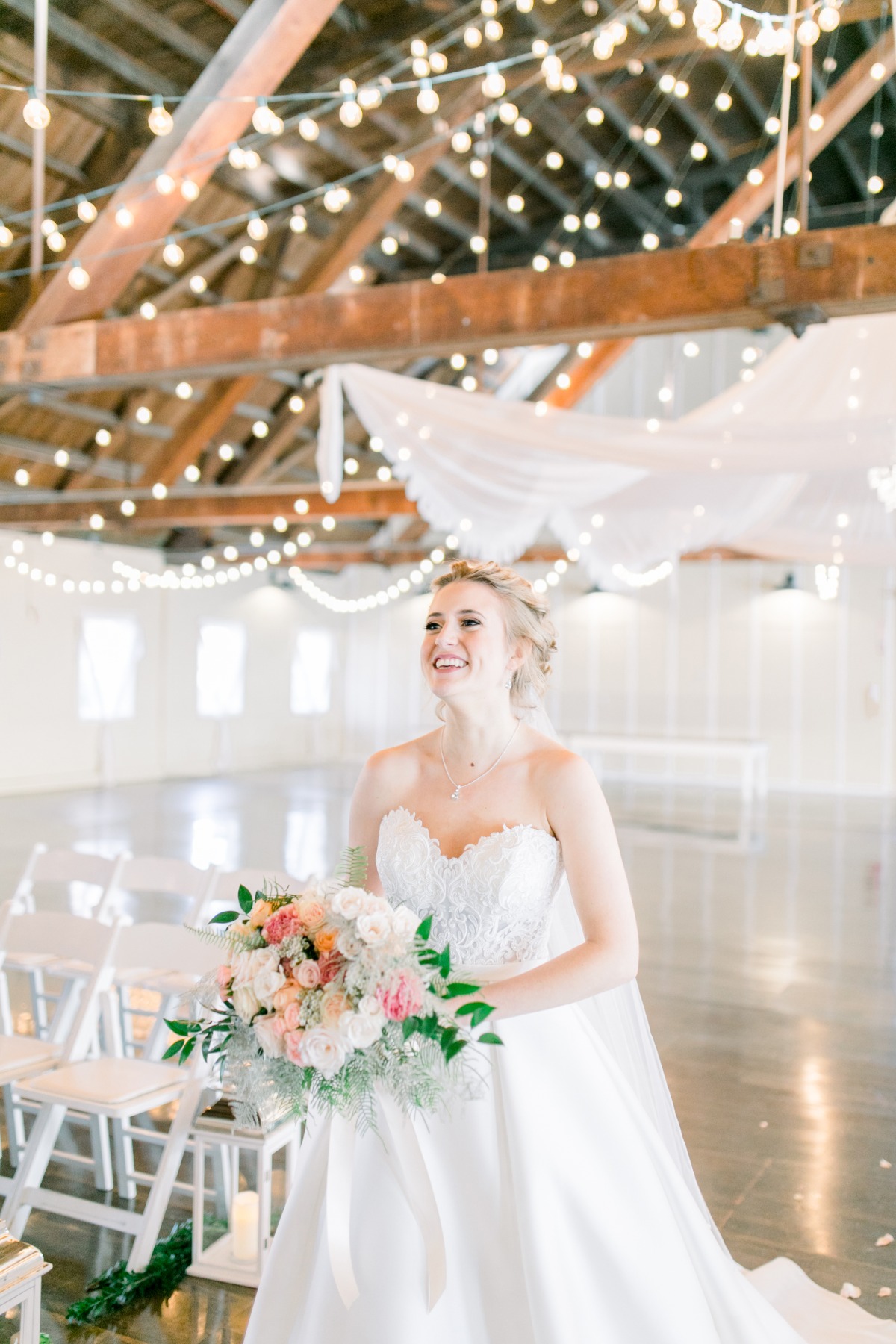 Happy bride holds flowers in wedding dress barn venue