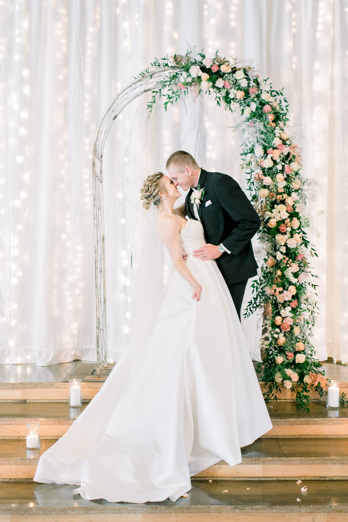 Bride and groom kissing under floral arch at wedding ceremony