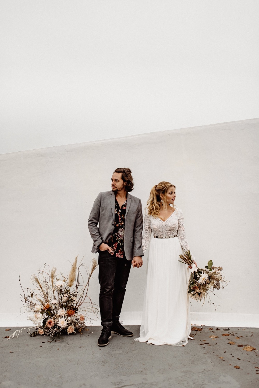 Bohemian wedding couple holding hands looking away, styled in love