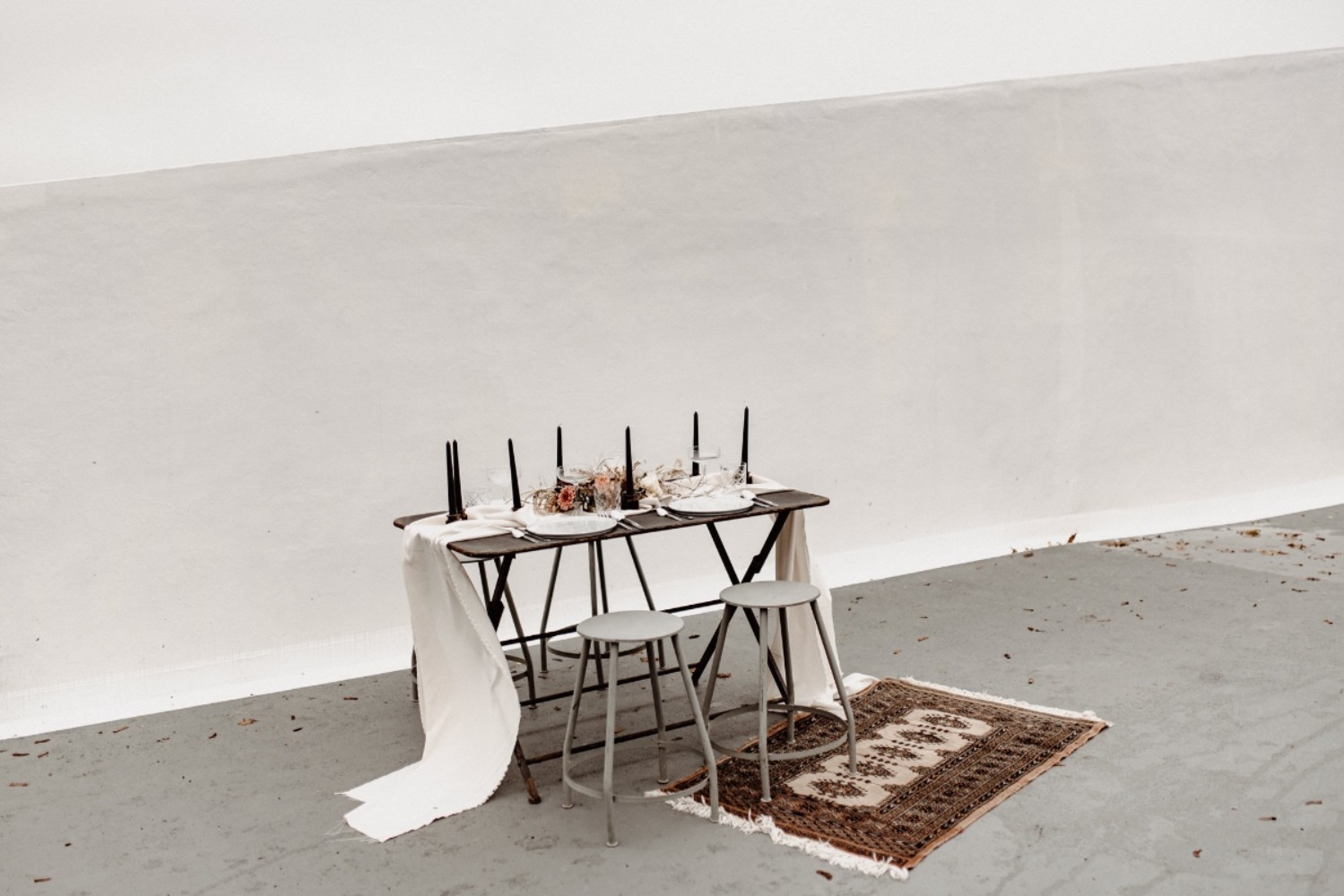 Minimalist outdoor table setting with candles, flowers, and rug