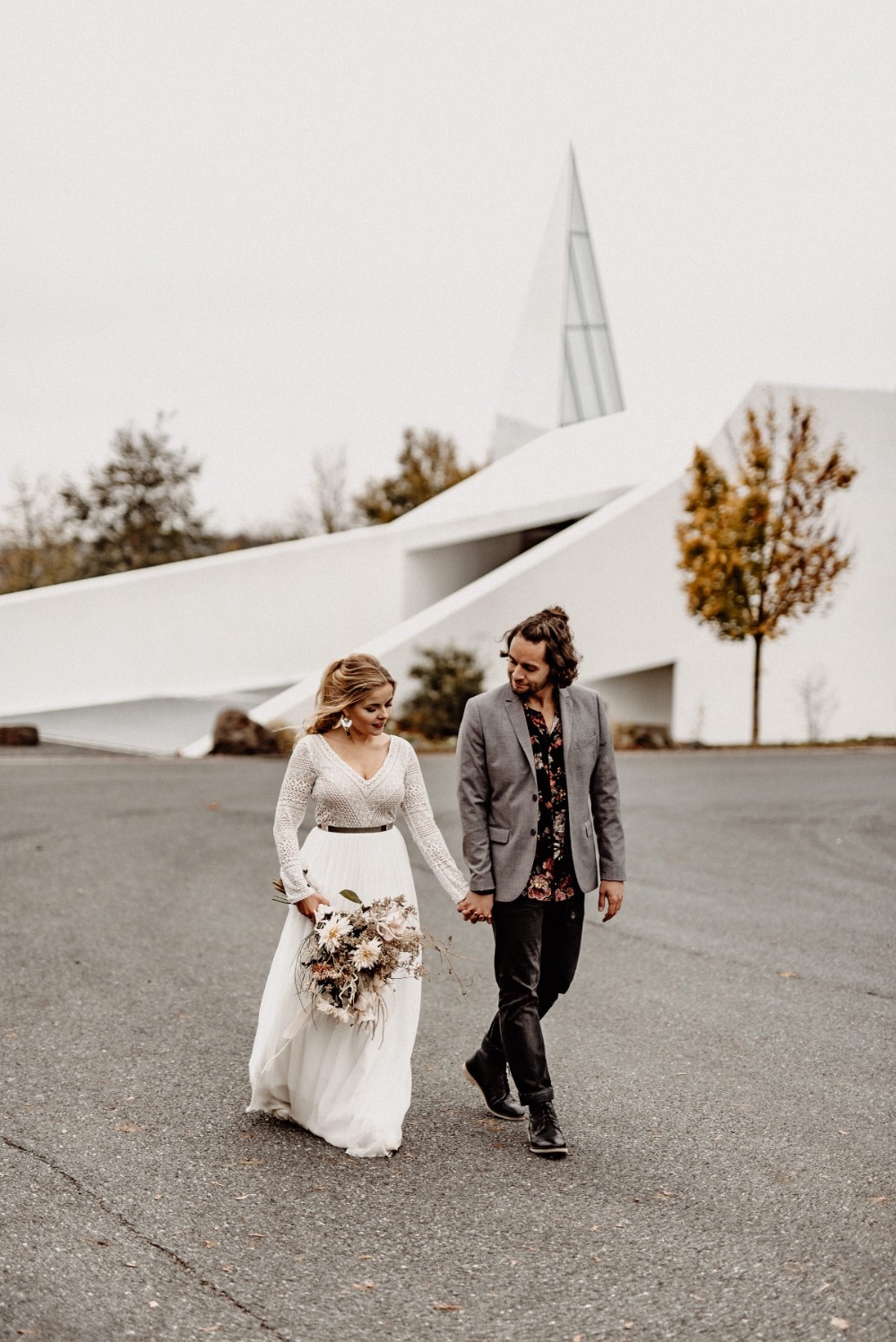 Newlyweds holding hands walking in front of a modern wedding venue