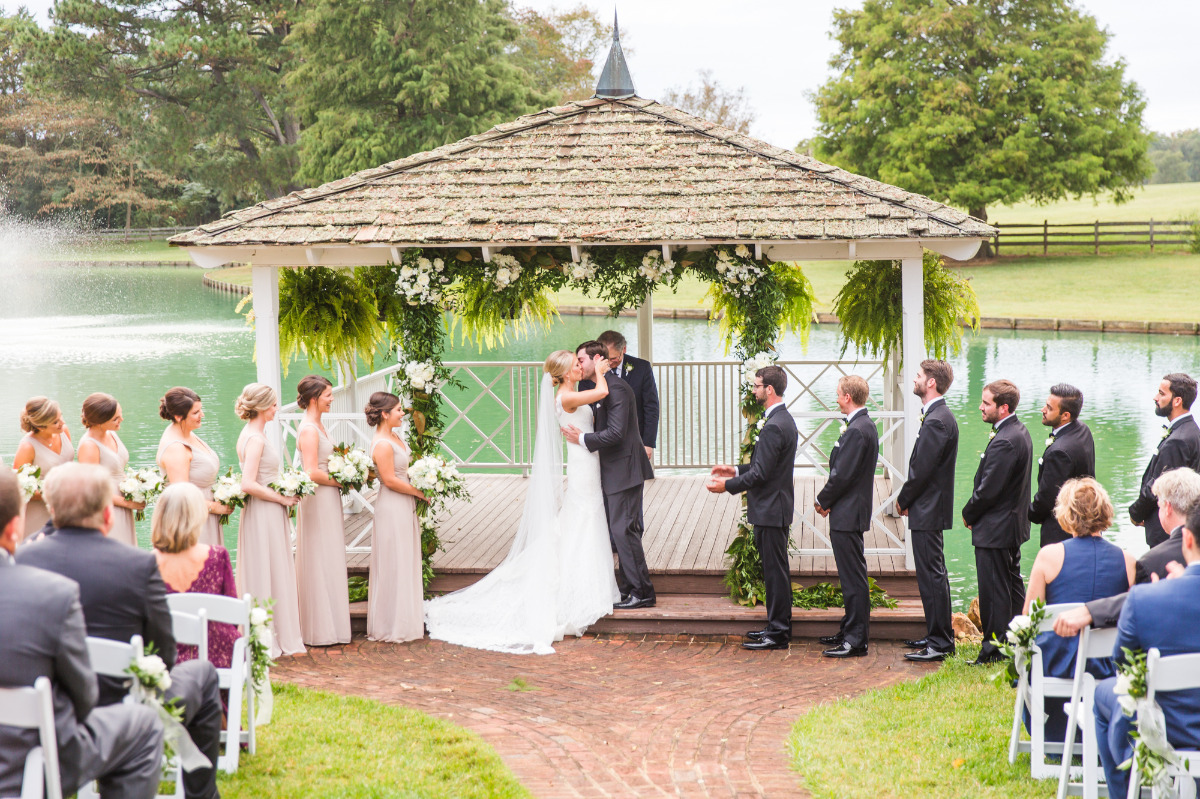 Outdoor wedding ceremony by a pond in a white gazebo