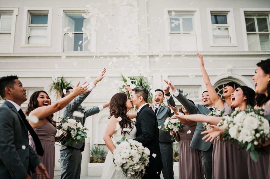 Happy couple kisses amidst flower petals thrown by wedding party