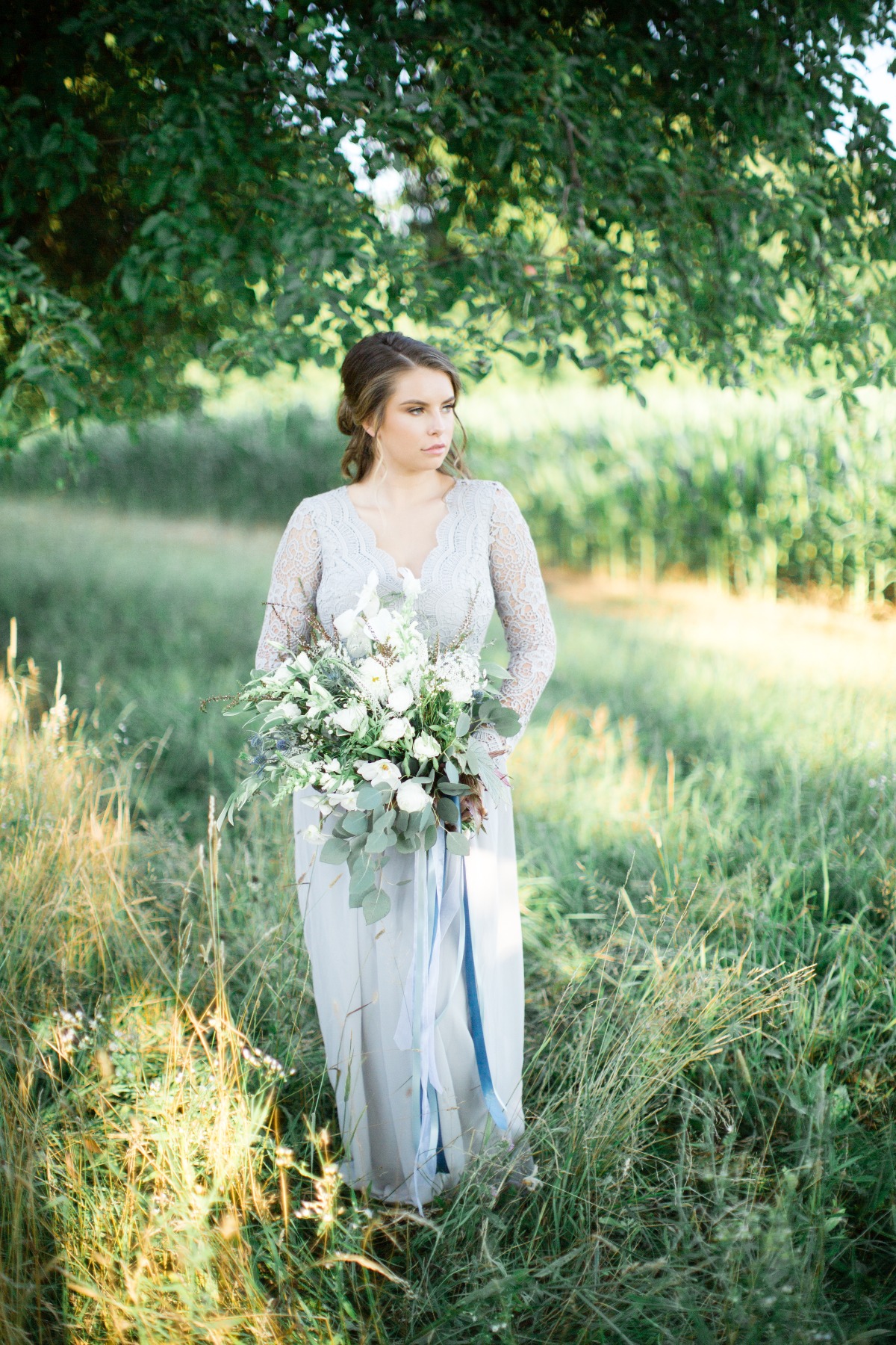 Bride in lace gown holds white floral bouquet outdoors