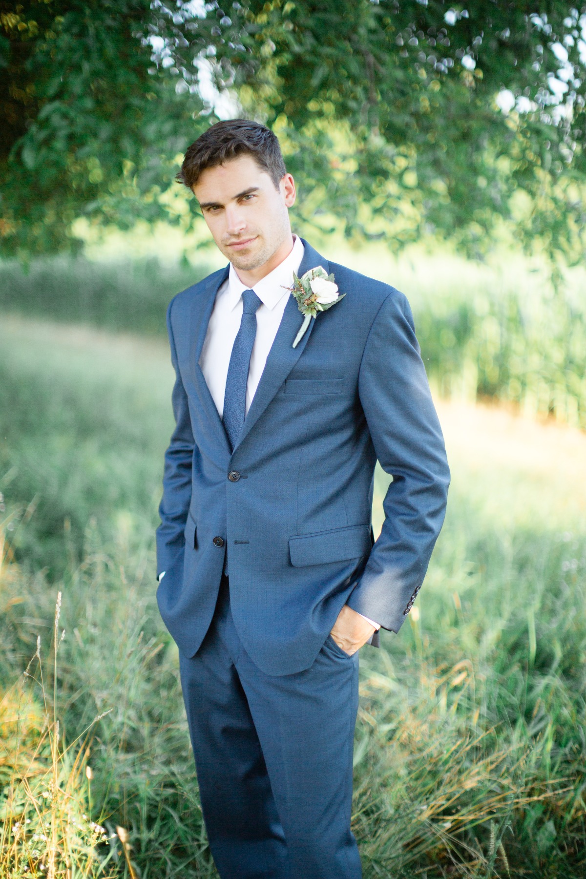 Handsome groom in blue suit poses with a floral boutonniere